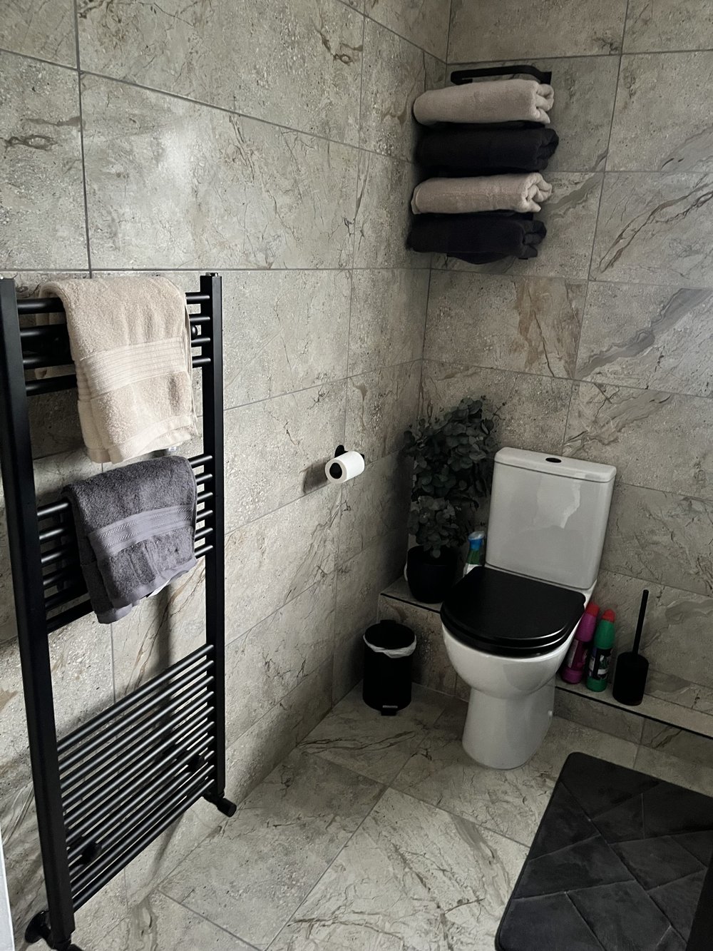 The same renovated bathroom with a black heated towel rail and a toilet with a black seat